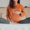 Pregnant woman sitting in crossed legs in be at home holding her belly