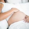 Pregnant woman embracing her belly while resting in bed