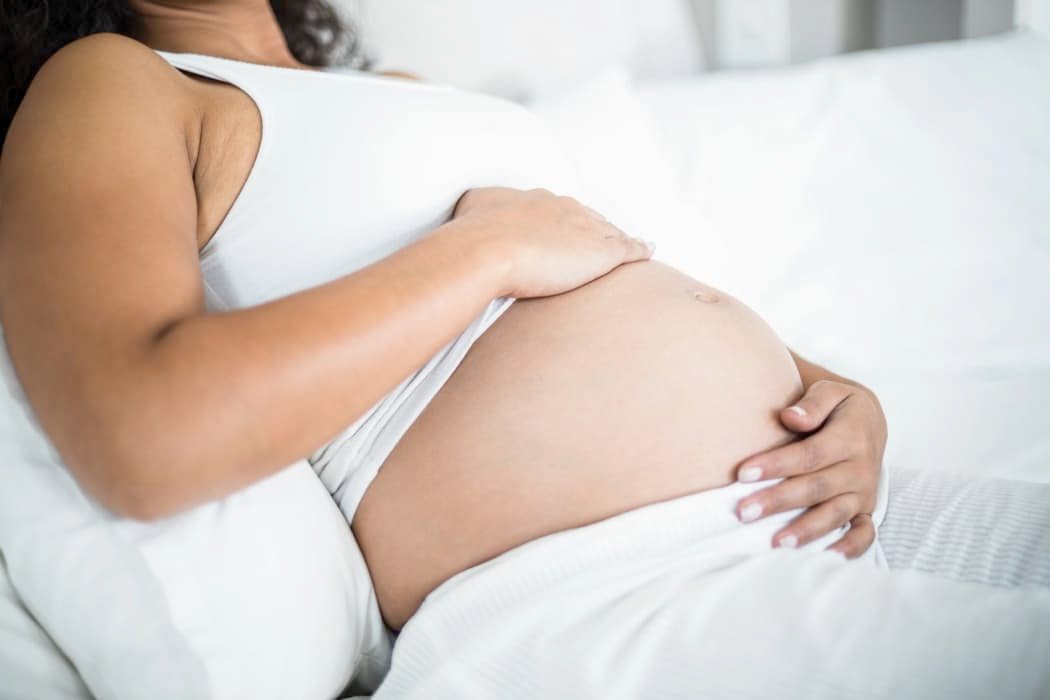Pregnant woman embracing her belly while resting in bed